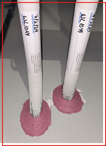 Two pipes pass through a wall, sealed with pink firestop material
